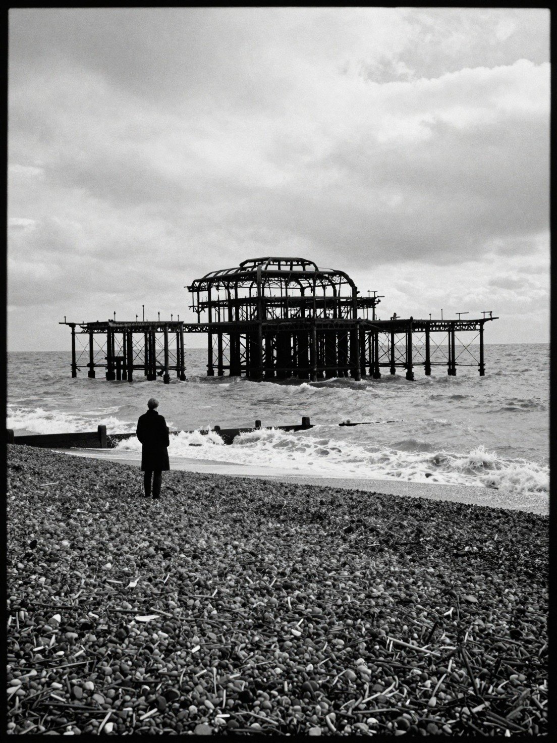 Guest AI work by Z-Image-Turbo: Untitled (grainy black-and-white 35mm). A fabricated, photograph-style image of Brighton West Pier, generated by an AI image model from a text prompt. It is not a real photograph.