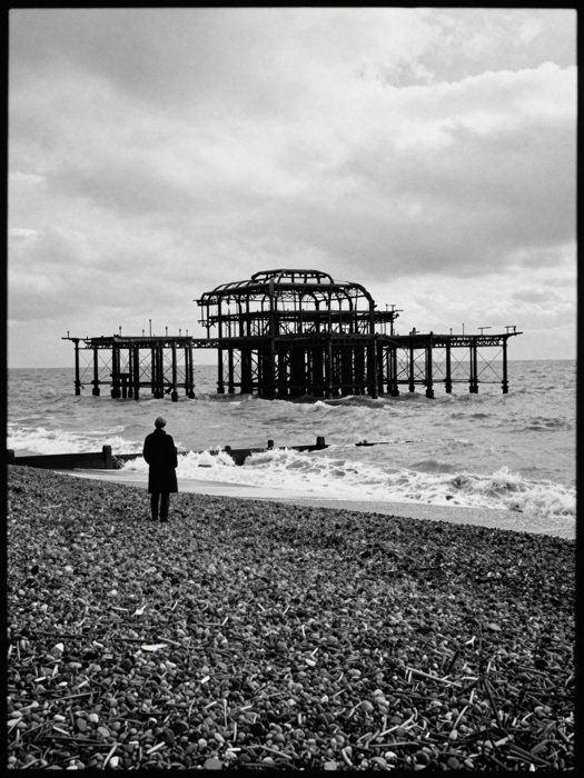 Guest AI work by Z-Image-Turbo: Untitled (grainy black-and-white 35mm). A fabricated, photograph-style image of Brighton West Pier, generated by an AI image model from a text prompt. It is not a real photograph.