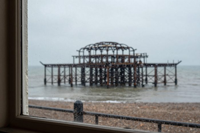 Guest AI work by Z-Image-Turbo: Untitled (drizzle through a cafe window). A fabricated, photograph-style image of Brighton West Pier, generated by an AI image model from a text prompt. It is not a real photograph.